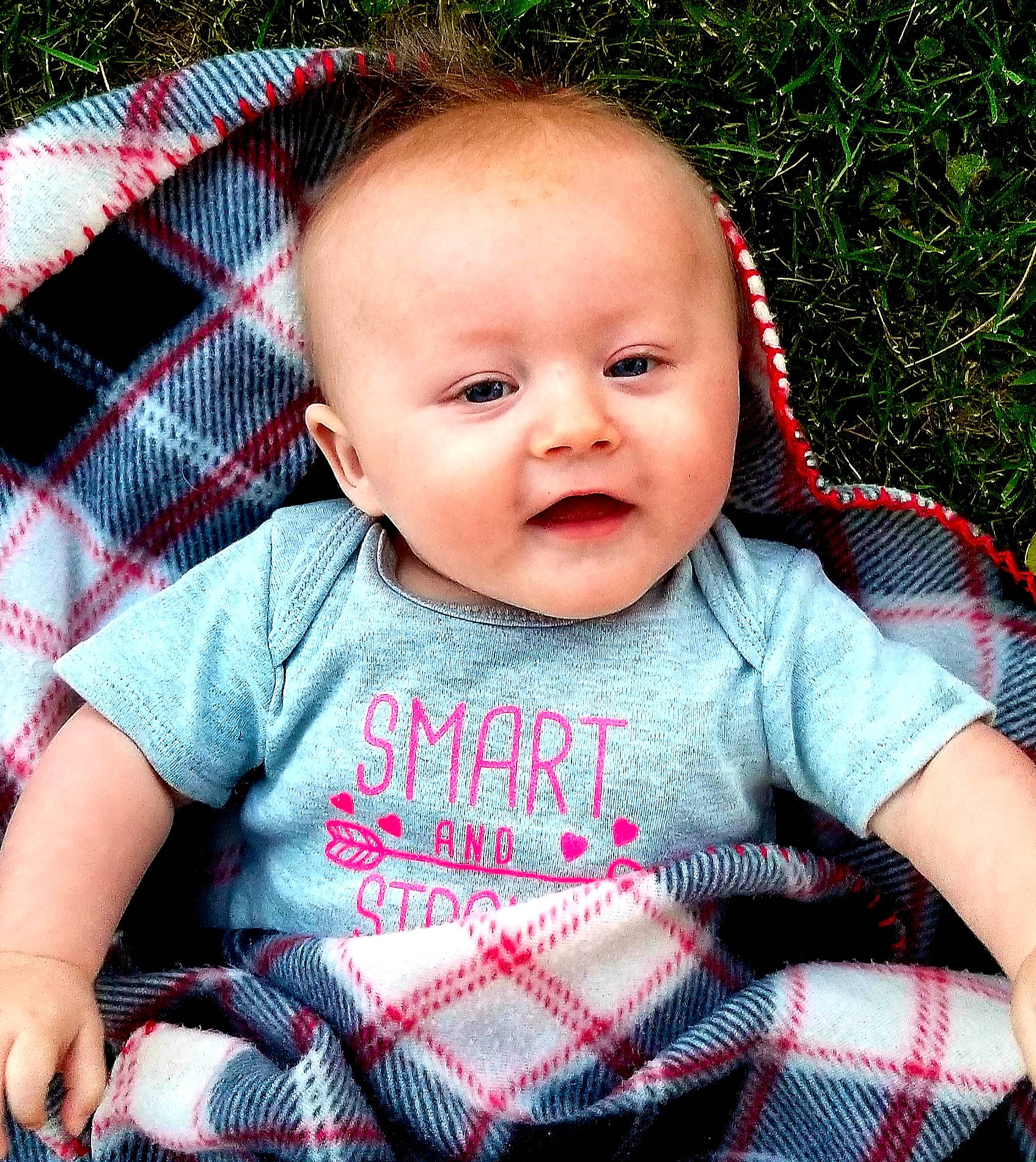 Timberlyn is registered to the contest to win money with this photo: baby, baby_products, baby_toddler_clothing, cheek, child, design, face, grass, head, lip, pattern, person, pink, plaid, product, sitting, skin, smile, tartan, textile