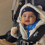 Phoenix is registered to the contest to win money with this photo: baby, child, smiling, stroller, jacket, headband, blue_clothing, jeans, footwear, indoor, seatbelt, happy, cute, portrait, person, infant, babywear, warm_clothing, face, hands