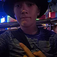 Ethanrodick joined the competition — help win amazing prizes! child, person, hat, bucket_hat, finger, pointing, striped_shirt, indoor, neon_lights, arcade, entertainment, young, face, headwear, casual_clothing, metal_railings, dark, blue_lighting, portrait, expression
