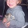 Roman is registered to the contest to win money with this photo: child, curly_hair, smiling, kitten, cat, grey_tracksuit, nike, sitting, indoor, red_eye, happy, holding, cute, pet, young, person, carpet, floor, casual_clothing, portrait