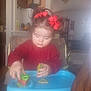 toddler, child, red_bows, magnetic_shapes, blue_tray, cocomelon, indoor, home, high_chair, playing, toy, concentration, furniture, clock, chair, table, living_room, sweater, hair, person