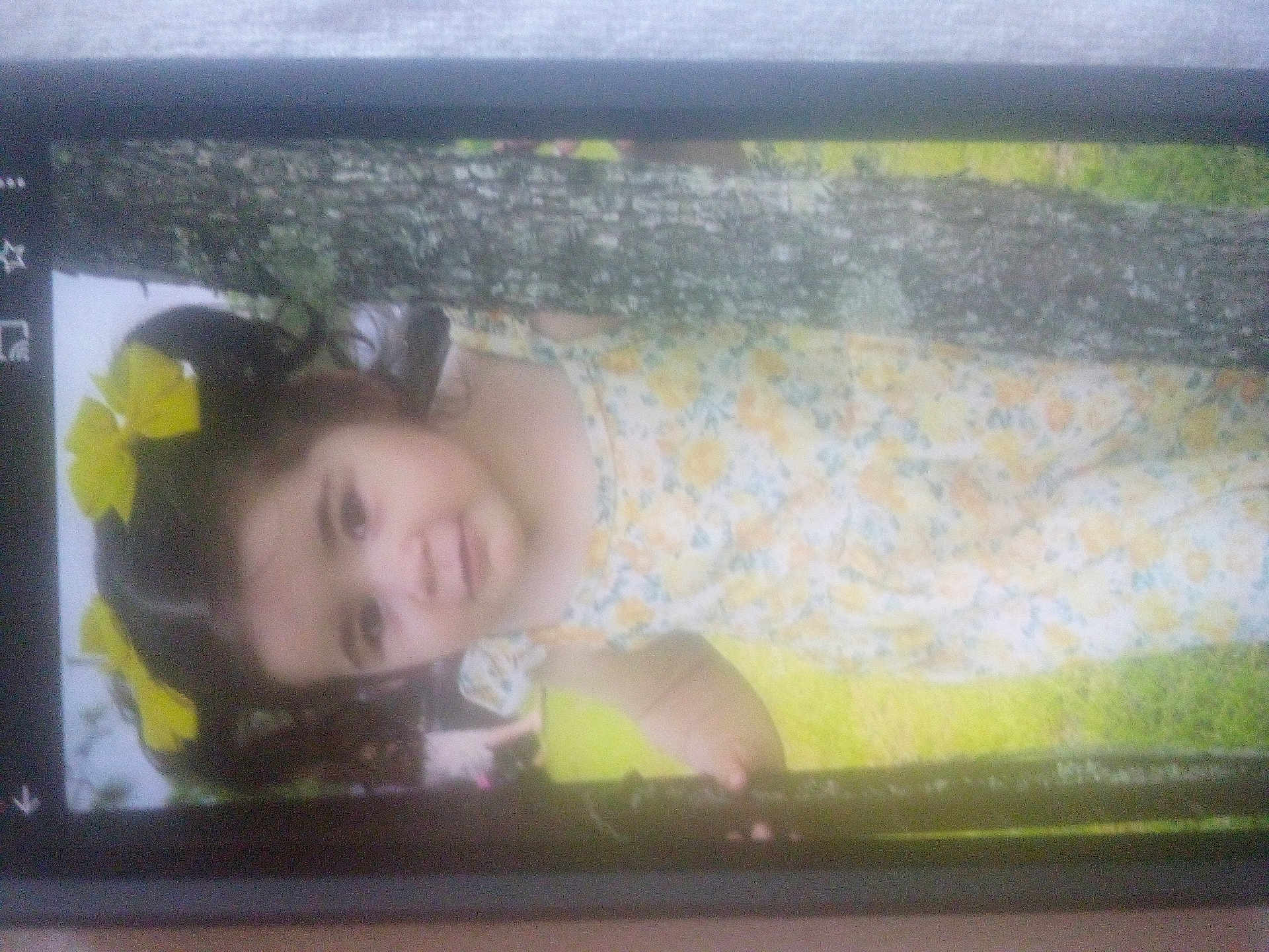 Emmy Ray is registered to the contest to win money with this photo: child, girl, yellow_bows, floral_dress, tree, grass, outdoor, portrait, young_child, nature, person, smile, hair, cute, summer, daylight, photo_of_photo, phone_screen, standing, holding