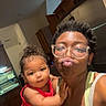 Layla is registered to the contest to win money with this photo: person, baby, child, glasses, kitchen, indoor, holding, smiling, red_clothing, tank_top, curly_hair, cabinet, refrigerator, home, family, portrait, cute, funny_face, affection, casual