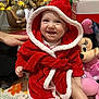 Ariyah joined the competition — help win amazing prizes! baby, child, smiling, red_hooded_robe, christmas_tree, holiday_decorations, plush_toy, minnie_mouse, festive, indoors, carpet, hand, toy, face, cute, sitting, happy, holiday, christmas, warm_clothing