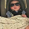 Wilder is registered to the contest to win money with this photo: baby, sunglasses, car_seat, blanket, child, infant, seat_belt, clothing, person, cute, face, head, sitting, fashion_accessory, patterned_blanket, indoors, safety, resting, adorable, young_child