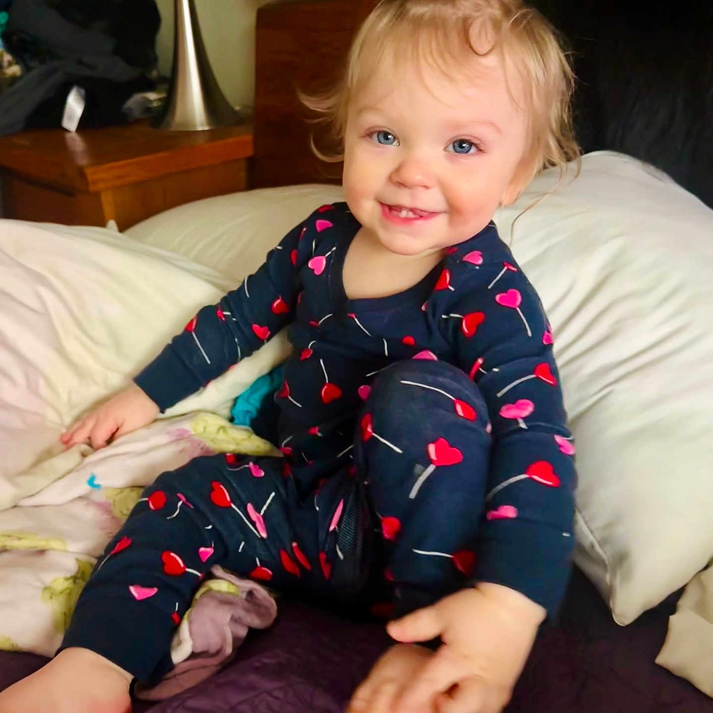 Rose is registered to the contest to win money with this photo: bed, blanket, blue_eyes, child, cute, face, foot, furniture, hair_tie, hand, happy, heart_pattern, indoor, lamp, nightwear, pajamas, person, smiling, toddler, wooden