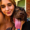 woman, dog, portrait, smiling, close_up, tattoo, nose_ring, tongue_out, pet, leash, outdoor, brick_wall, porch, happy, friendship, face, skin, hair, collar, warm_light