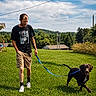 Penelope is registered to the contest to win money with this photo: man, dog, leash, grass, field, outdoor, sky, clouds, casual_clothing, shorts, tshirt, walking, pet, canine, happy, nature, summer, daylight, greenery, recreation