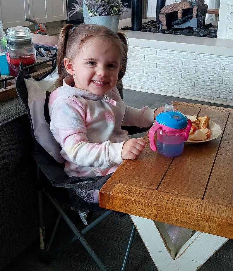 Avyahna is registered to the contest to win money with this photo: baby_toddler_clothing, chair, child, food, fun, furniture, happy, joy, kitchen_dining_room_table, leisure, outdoor_furniture, outdoor_table, person, picnic_table, room, sharing, sitting, smile, table, tableware