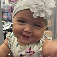 Alaina is registered to the contest to win money with this photo: accessory, apparel, arm, baby, butterfly, child, closeup, cute, dress, flower, happy, headband, holding, indoor, infant, person, portrait, smiling, store, tattoo