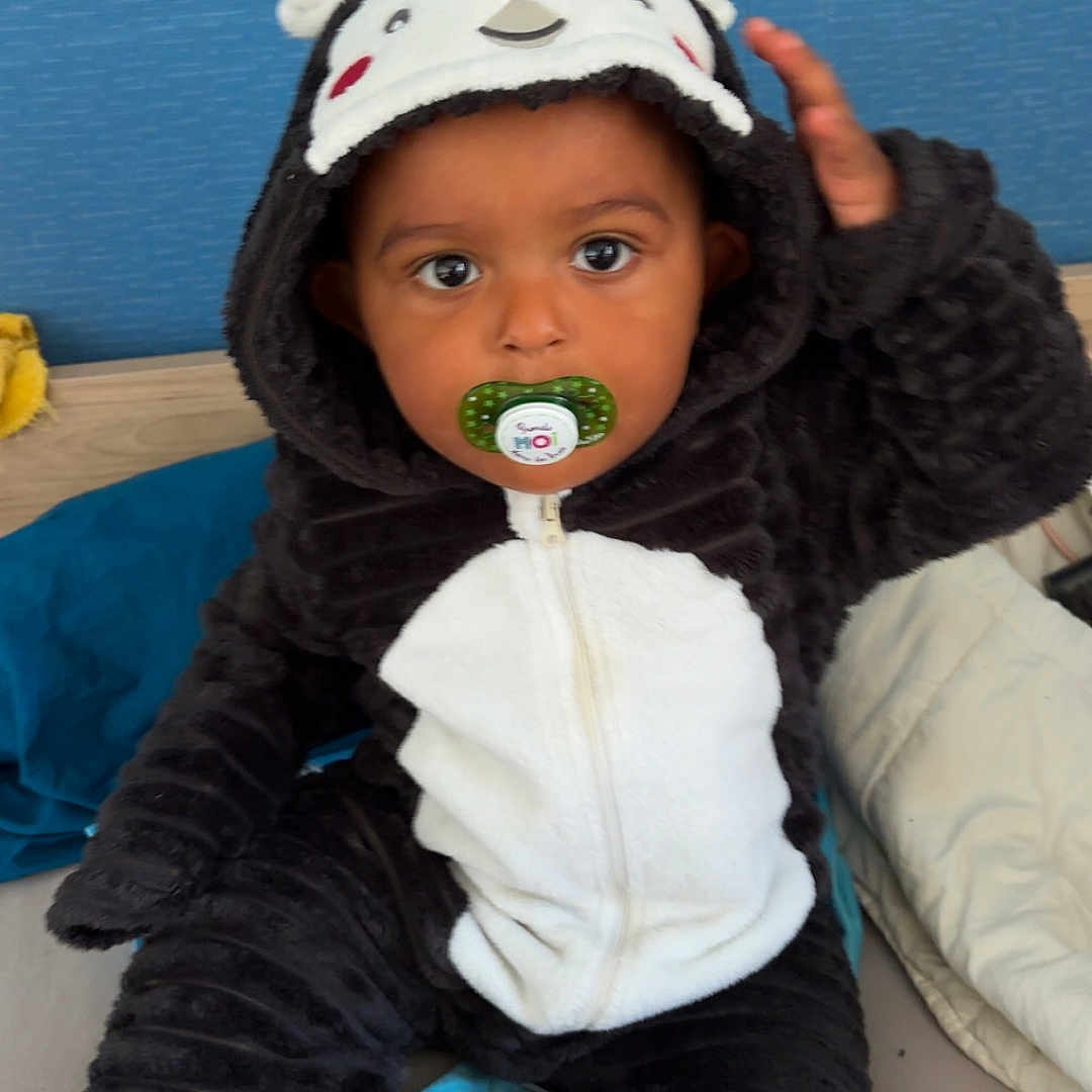 Oweynn participe au concours pour gagner de l'argent avec cette photo : bed, beige_blanket, black_and_white, blue_background, child, clothing, costume, cute, eyes, face, hand, hood, indoor, onesie, pacifier, plush, portrait, sitting, soft, toddler