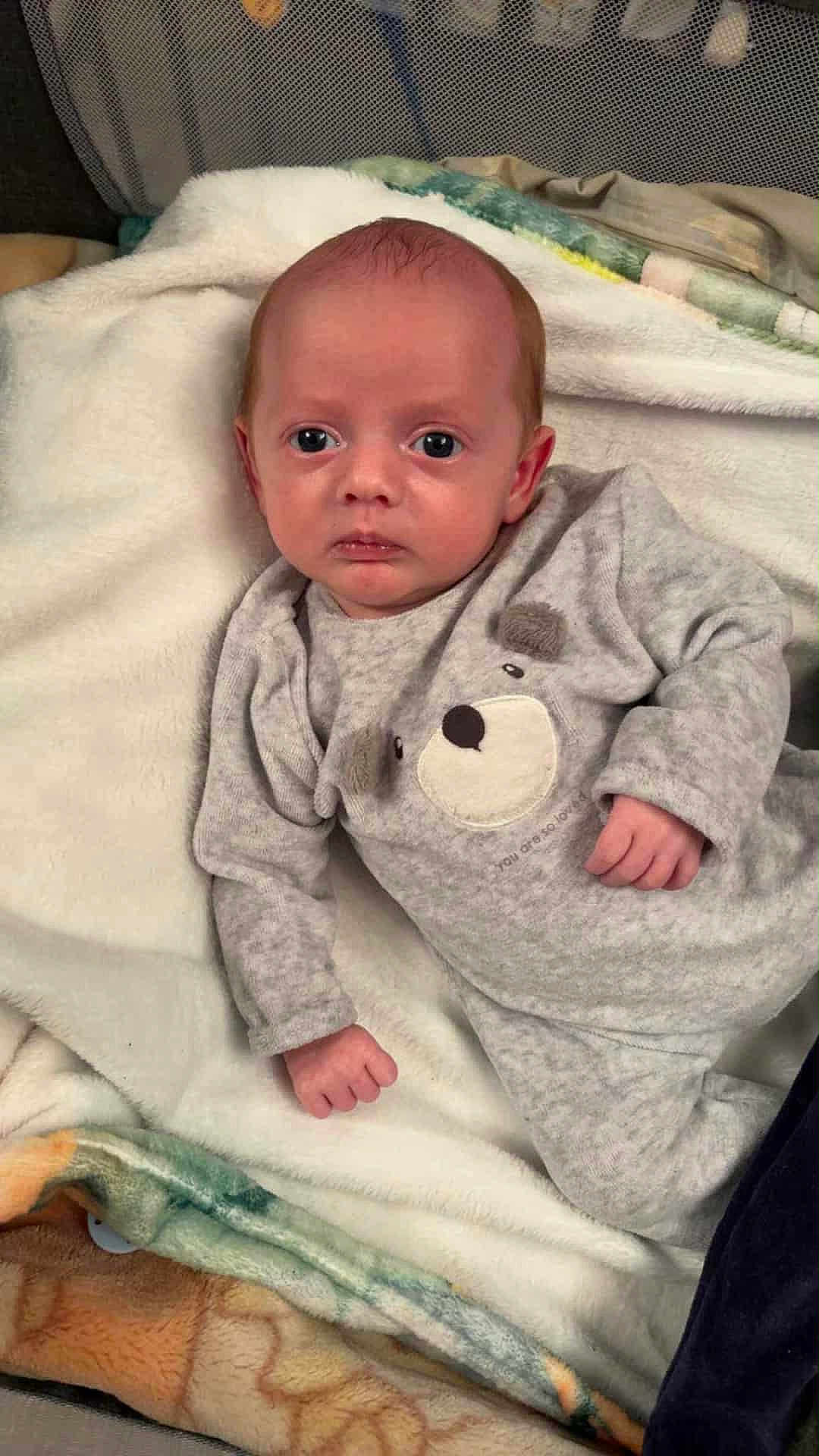 Maloé a rejoint le concours — aidez-le/la à gagner de superbes lots ! baby, infant, onesie, gray_clothing, bear_design, blanket, fluffy_blanket, lying_down, indoors, face, hand, head, expression, curious, child, newborn, soft_texture, person, cozy, sleepwear