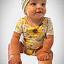 baby, child, headband, bow, onesie, sunflower, floral, sitting, hands, feet, portrait, cute, blue_eyes, soft_background, indoor, infant, smiling, skin, clothing, person