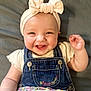 baby, smiling, child, headband, bow, denim_overalls, clothing, floral_skirt, happy, face, skin, infant, cute, person, portrait, baby_girl, sitting, hand, indoors, soft_background