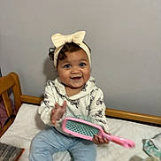 Honesty joined the competition — help win amazing prizes! baby, child, infant, sitting, smiling, happy, bow, headband, hairbrush, toy, bed, bedroom, indoors, portrait, face, eyes, clothing, pants, furniture, bottle