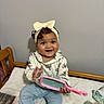 baby, child, infant, sitting, smiling, happy, bow, headband, hairbrush, toy, bed, bedroom, indoors, portrait, face, eyes, clothing, pants, furniture, bottle