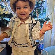 Zean participe au concours pour gagner de l'argent avec cette photo : child, toddler, smiling, hat, traditional_clothing, white_outfit, vest, indoor, christmas_tree, holiday_decorations, toy, happy, curly_hair, festive, home, celebration, curtains, furniture, living_room, decor