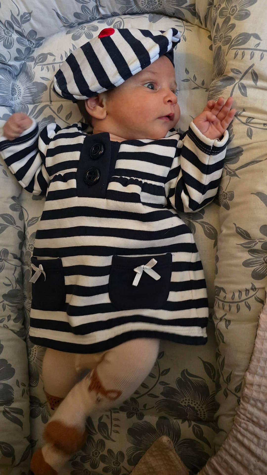 Cataleya participe au concours pour gagner de l'argent avec cette photo : baby, beret, child, comfort, curious_expression, cushion, cute, dress, face, floral_pattern, hand, indoors, infant, lying_down, person, portrait, small_hands, soft_lighting, striped_clothing, tights