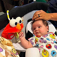 Saylor joined the competition — help win amazing prizes! baby, infant, child, portrait, sitting, bouncer, elmo, plush_toy, sesame_street, colorful_clothing, onesie, wide_eyed, indoor, home, desk, computer, adult_hand, hand, toy, happy
