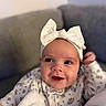 Saylor is registered to the contest to win money with this photo: baby, infant, child, smiling, face, portrait, headband, bow, white_bow, floral_clothing, onesie, pajamas, blanket, plush_blanket, couch, indoor, close_up, happy, cozy, nursery