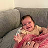 Saylor is registered to the contest to win money with this photo: baby, infant, child, smiling, happy, portrait, close_up, indoors, couch, blanket, pink_blanket, clothing, hand, adult_hand, tattoo, ring, sitting, reclining, home, family