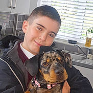Nala is registered to the contest to win money with this photo: boy, dog, pet, indoor, kitchen, window, smile, child, animal, cute, collar, black, brown, face, human, holding, happy, casual, hoodie, portrait