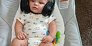 Theo is registered to the contest to win money with this photo: baby, infant, headphones, onesie, baby_seat, carpet, toy, footwear, couch, child, person, sitting, cute, indoor, plush, relaxed, music, audio, chubby, comfort