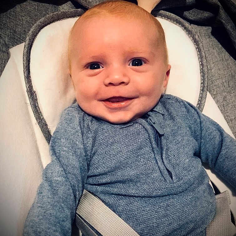 Michael is registered to the contest to win money with this photo: baby, baby_seat, blue_eyes, blue_sweater, child, close_up, clothing, comfort, cozy, cute, expression, face, happy, indoor, infant, person, portrait, seat, smiling, straps