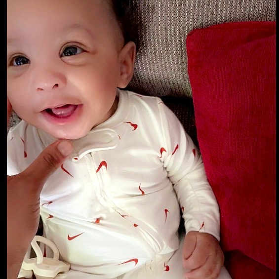 Remaje joined the competition — help win amazing prizes! baby, infant, smiling, onesie, white_clothing, red_pattern, couch, pillow, hand, face, happy, child, indoors, cute, portrait, young, person, seated, fabric, texture
