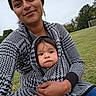 Adrian Zelaya joined the competition — help win amazing prizes! baby, infant, mother, parent, child, portrait, outdoor, park, soccer_field, goalpost, grass, trees, family, 抱抱, wearing_wrap, patterned_clothing, smiling, sitting, closeup, photography