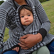 Adrian Zelaya is registered to the contest to win money with this photo: baby, infant, child, portrait, face, looking_at_camera, serious_expression, outdoor, park, grass, adult, parent, holding, cuddling, blanket, knitwear, hood, sweater, hand, family