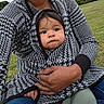 baby, infant, child, portrait, face, looking_at_camera, serious_expression, outdoor, park, grass, adult, parent, holding, cuddling, blanket, knitwear, hood, sweater, hand, family