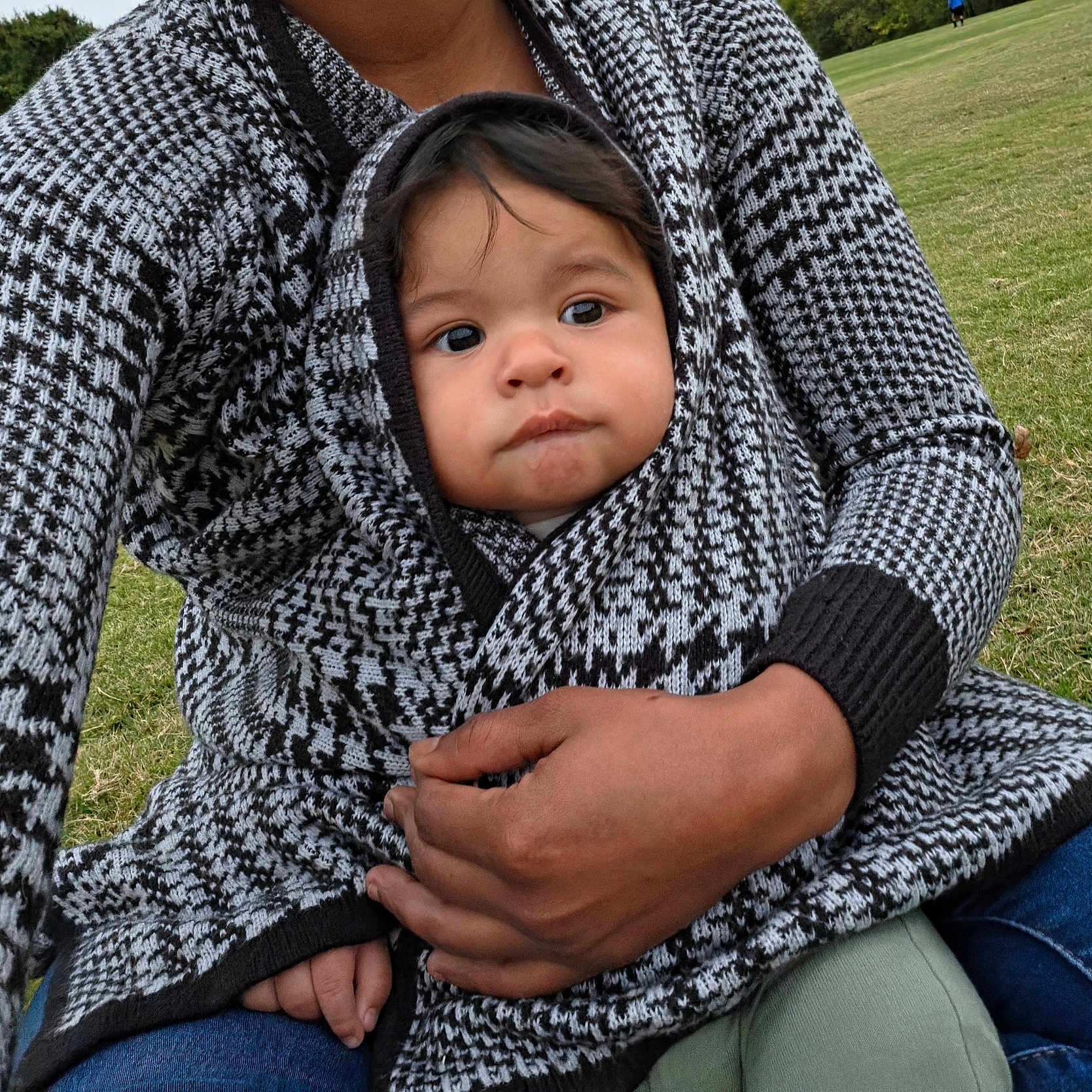 Adrian Zelaya is registered to the contest to win money with this photo: baby, infant, child, portrait, face, looking_at_camera, serious_expression, outdoor, park, grass, adult, parent, holding, cuddling, blanket, knitwear, hood, sweater, hand, family