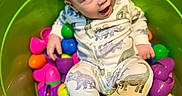 Jace is registered to the contest to win money with this photo: baby, child, bucket, green, colorful, plastic_eggs, pajamas, dinosaur_print, sitting, happy, indoor, play, cute, face, footwear, smile, toy, bright_colors, infant, curious