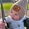 baby, child, hat, knit_hat, bear_patch, swing, playground, outdoor, daylight, infant, cute, warm_clothing, grip, face, portrait, young_child, curious, soft_light, closeup, blurred_background