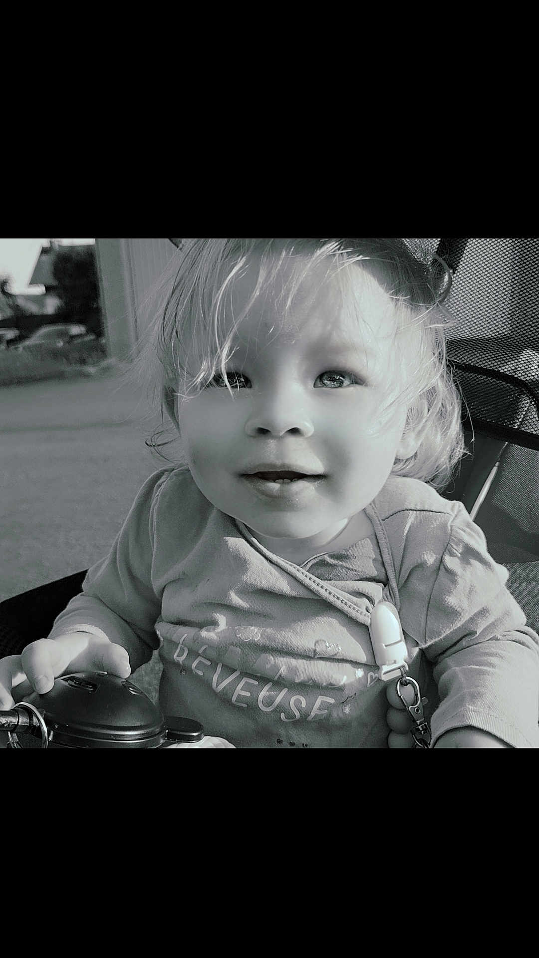 Zélia a rejoint le concours — aidez-le/la à gagner de superbes lots ! baby, black_and_white, child, closeup, clothing, curly_hair, cute, expression, face, hair, hand, infant, outdoor, portrait, seat, smile, stroller, sunlight, toddler, toy