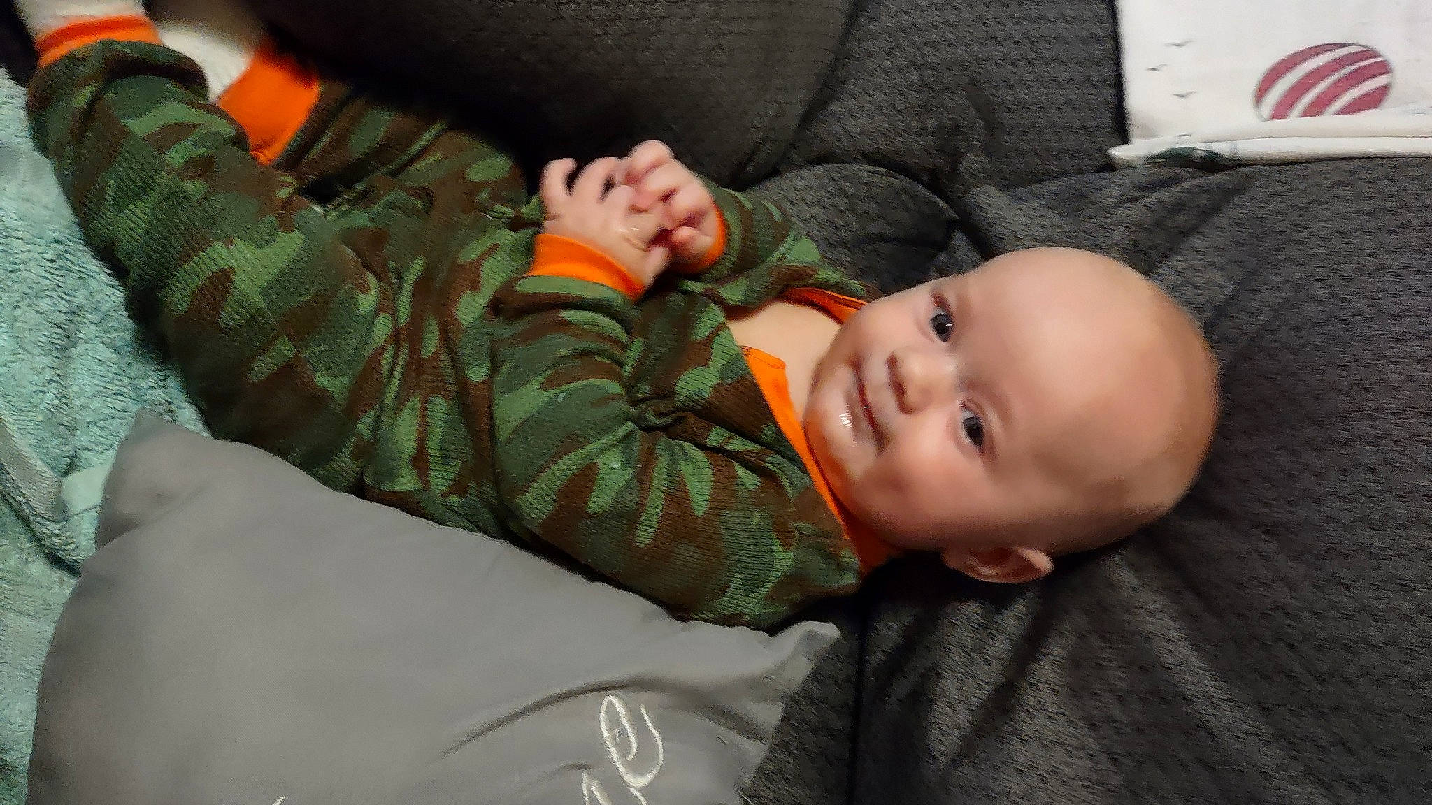 Asa is registered to the contest to win money with this photo: baby, baby_toddler_clothing, cheek, child, comfort, finger, gesture, happy, military_camouflage, person, sitting, skin, sleeve, smile, thumb, toddler, tree, wood