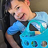 child, boy, smiling, car, seatbelt, blue_shirt, basket, snacks, happy, portrait, window, seat, daylight, casual, young, cute, interior, person, playful, travel