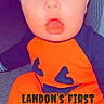 Landon is registered to the contest to win money with this photo: baby, child, halloween, costume, orange_clothing, black_clothing, face, expression, sitting, floor, indoors, carpet, cute, young_child, holiday, festive, portrait, person, text_overlay, timestamp