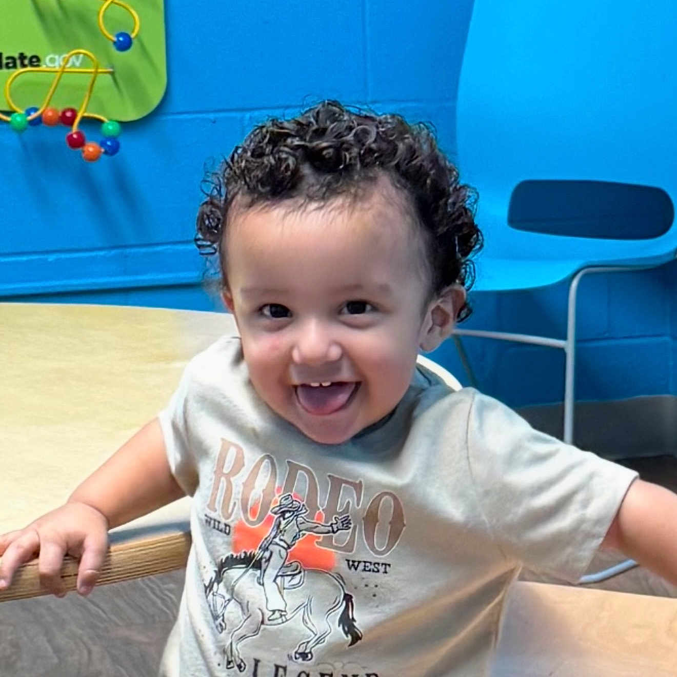 Joseph Jacob Jr joined the competition — help win amazing prizes! blue_wall, casual_clothing, chair, child, curly_hair, cute, expression, fun, happy, indoor, leisure, person, playroom, smiling, table, toddler, tongue_out, toy, tshirt, young_child