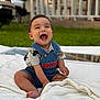 baby, child, smiling, laughing, sitting, outdoor, blanket, denim_overall, mickey_mouse, shirt, grass, porch, vehicle, foot, hand, person, face, happy, clothing, daylight