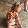 baby, barefoot, blond_hair, blue_eyes, bread, candid, chairs, child, concrete_floor, diaper, eating, face, food, hands, happy, home, indoor, infant, portrait, sitting