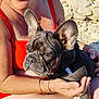 Arley participe au concours pour gagner de l'argent avec cette photo : woman, dog, french_bulldog, puppy, sunglasses, red_swimsuit, outdoor, beach, rocks, sunlight, nature, pet, cuddling, happy, smiling, bracelet, tattoo, short_hair, summer, vacation