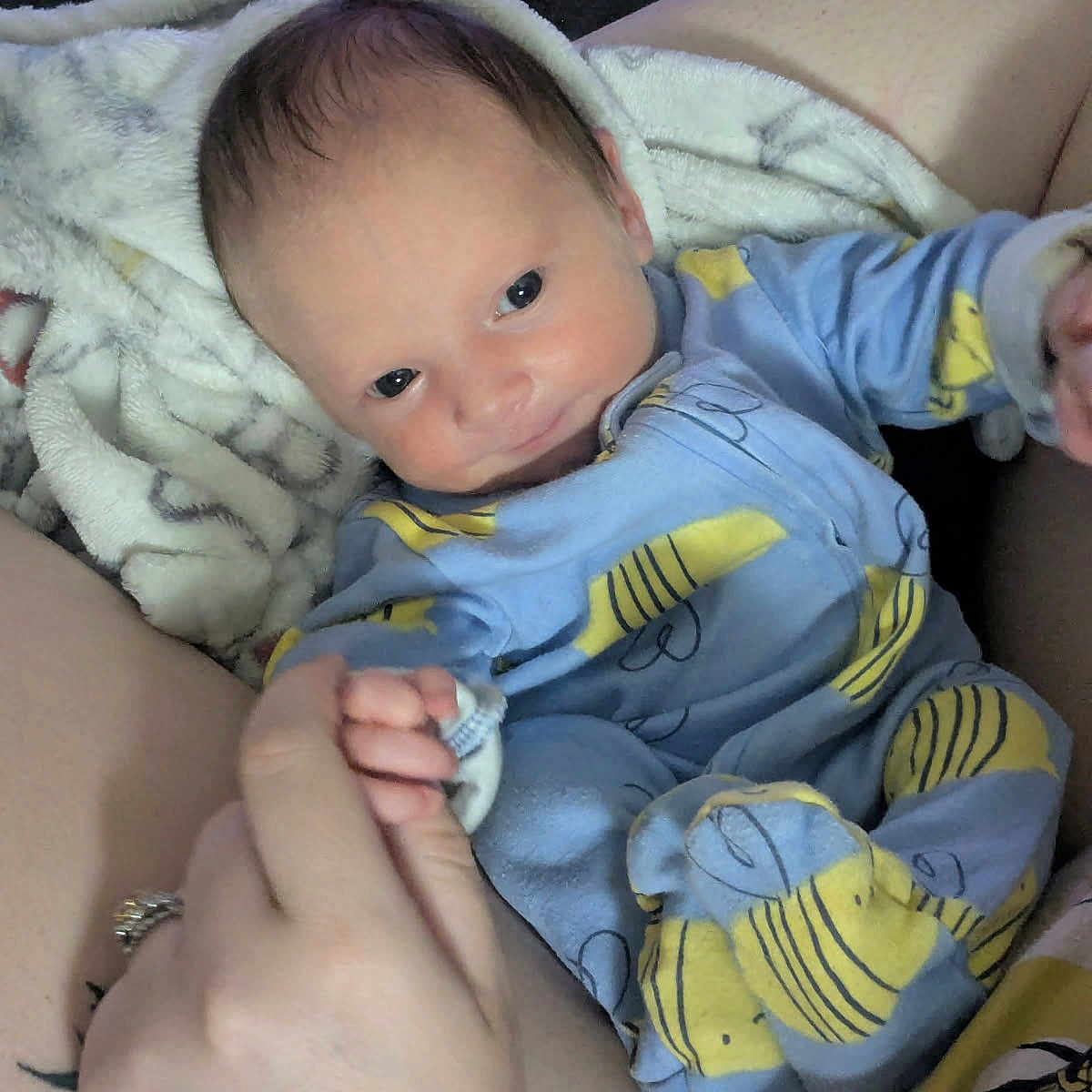Aurora joined the competition — help win amazing prizes! baby, infant, child, portrait, lying_down, blue_outfit, yellow_pattern, blanket, cozy, indoor, home, adult_arms, caregiver, wide_eyes, looking_at_camera, face, hands, clothing, soft_blanket, family