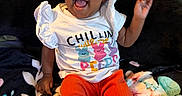 Victoria is registered to the contest to win money with this photo: baby, infant, child, smiling, laughing, sunglasses, portrait, sitting, blanket, bed, clothing, shirt, red_pants, shoes, colorful, indoor, cozy, happy, face, photography