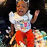 baby, infant, child, smiling, laughing, sunglasses, portrait, sitting, blanket, bed, clothing, shirt, red_pants, shoes, colorful, indoor, cozy, happy, face, photography