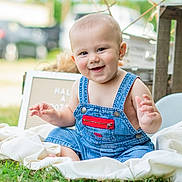 Preston joined the competition — help win amazing prizes! baby, denim_overalls, smiling, grass, blanket, outdoor, child, cute, happy, portrait, infant, sitting, face, person, casual_clothing, greenery, daylight, playful, young_child, red_zipper