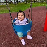 Anya is registered to the contest to win money with this photo: baby, child, swing, playground, smiling, happy, outdoor, park, grass, trees, clothing, jacket, pants, socks, person, seat, metal_chains, daylight, fun, cute