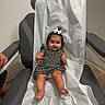 Anya joined the competition — help win amazing prizes! baby, child, smile, dress, bow, hair, medical_chair, paper_cover, indoor, floor, person, cute, chubby_cheeks, legs, feet, hand, arm, wall, room, waiting_room