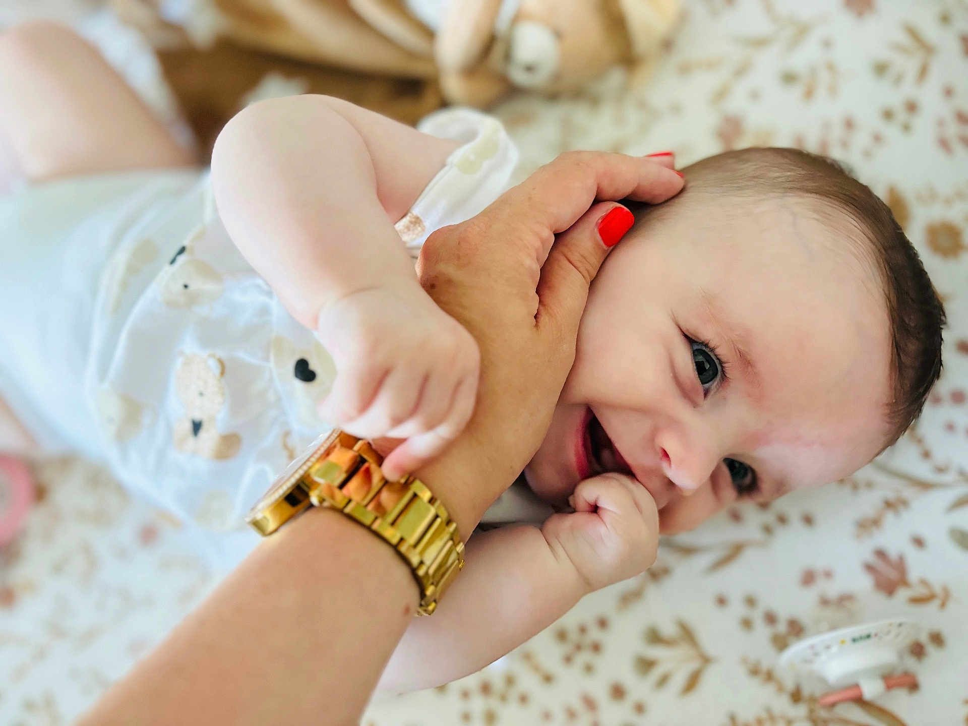 Héloïse a rejoint le concours — aidez-le/la à gagner de superbes lots ! adult_hand, baby, baby_girl, blanket, closeup, clothing, cute, face, hand, happy, infant, interaction, lying_down, nail_polish, pacifier, pattern, playful, skin, smile, watch